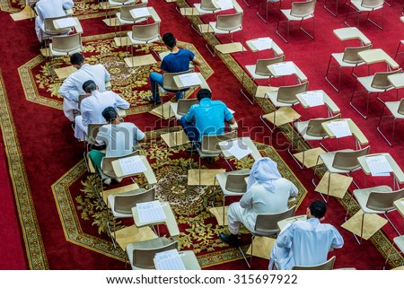 DAMMAM, SAUDI ARABIA -  JULY 8:  On a red carpet with rows of desks and chairs, college students prepare for an exam on 8 July, 2015 in Dammam, Saudi Arabia.