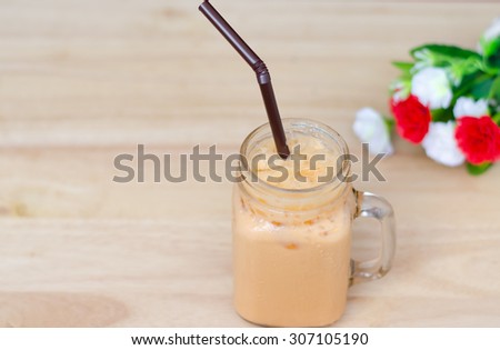 Ice milk tea with red and white  flower on wooden table