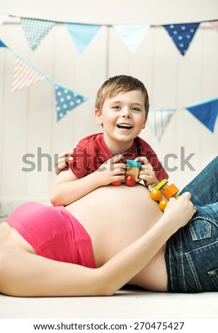 Happy childplaying next to belly of pregnant woman