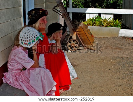 Three girls in period costume waiting at an old train station.
