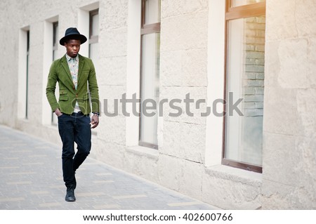 Fashion portrait of black african american man on green velvet jacket and black hat walking on streets of city background house with many windows