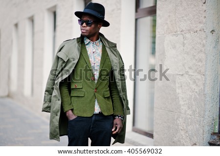 Fashion portrait of black african american man on green velvet jacket, black hat and coat cloak on his shoulders walking on streets of city background house with many windows