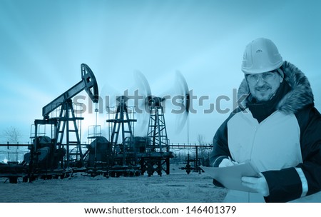 Oil worker in orange uniform and helmet on of background the pump jacks and sunset sky. Monochrome.