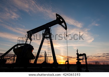 Silhouette oil pump jacks at sunset sky background.