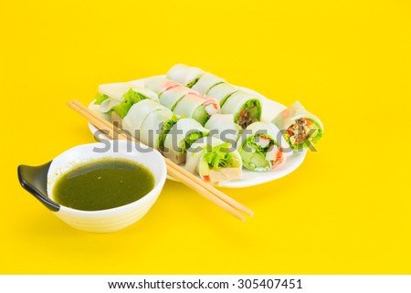 Portion of spring rolls on white dish with spicy sauce, vegetabl