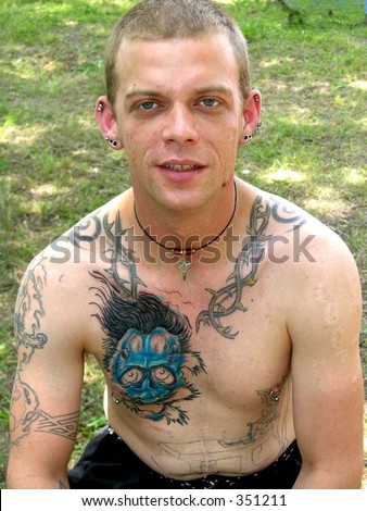 Young man heavily tattooed with pierced ears and nipples and knife wound scars