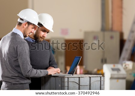 Two businessman working with laptop in factory.
