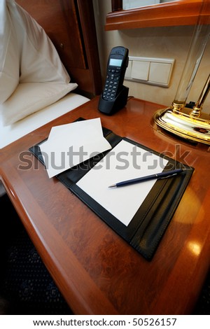 Night table with note book, pen and phone in a hotel room.