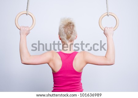 young woman gymnast competing on rings, back