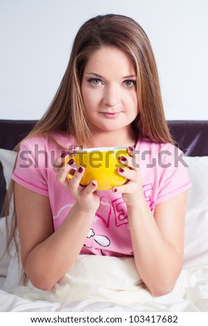 young woman sitting in bed and drinking a cup of tea