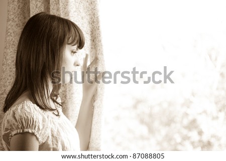 portrait of a cute young woman looking outside window - sepia