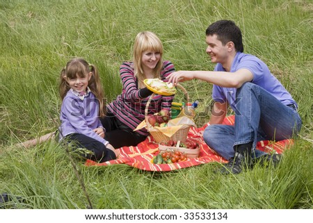 Family having picnic in park. Parents and child on picnic in the forest. Mother, father and daughter relaxing. Wife is giving husband sandwich.