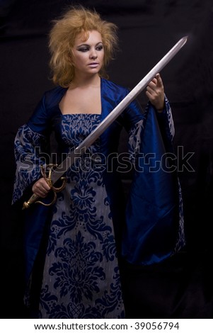 Woman in medieval  dress is holding weapon. Horrible witch with sword on black background.