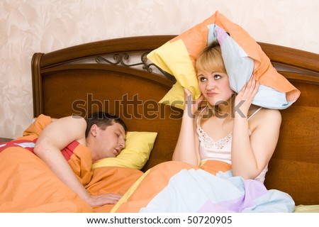 Male snoring on the bed and her wife can not sleep. Couple in bed with woman trying to sleep with man snoring. A young lady is having difficulty sleeping because of her man's snoring problem.