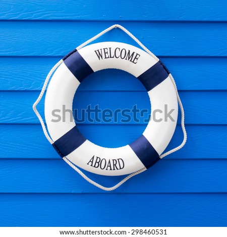 White Life buoy with welcome aboard on blue wall.