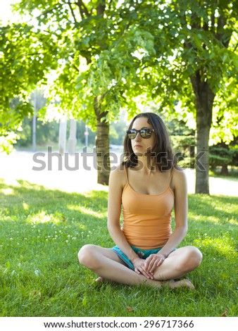 A young and quiet girl sitting resting on the green grass in the Park.