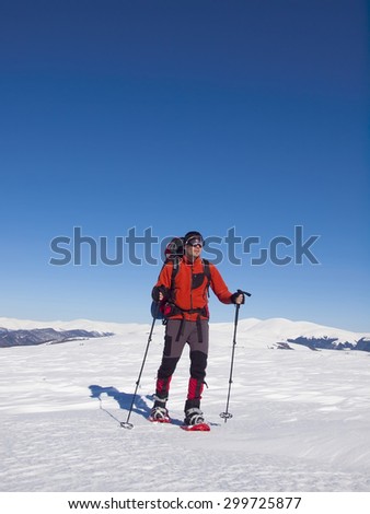 The man in snowshoes and with trekking poles is in the mountains.