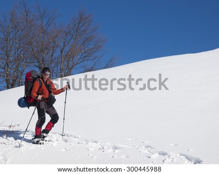 A man in snowshoes and a backpack is in the mountains in the snow.