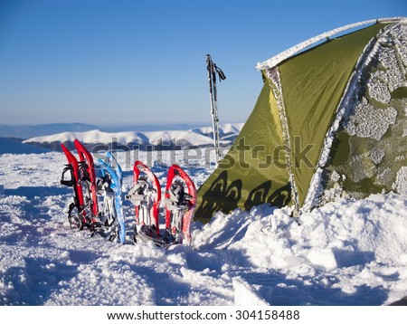 Snowshoes and snow-covered tent in the mountains against the blue sky.