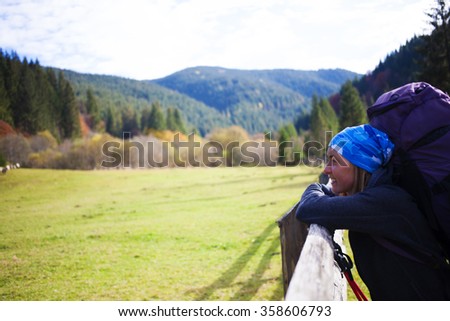 The girl with the backpack resting near wooden fence.