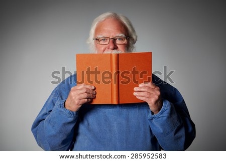 Portrait of senior man holding up a book and looking at the camera against grey background