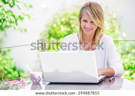 beautiful woman working on a computer at home with green garden on her background