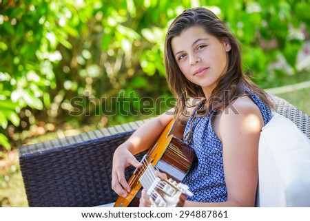 Portrait of very handsome teenager playing guitar in her garden