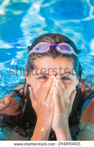 smiling teen in a pool puts her hands in front of her nose