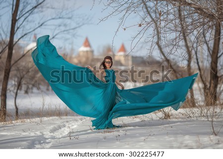 Beautiful girl in the mask in a flowing dress standing in the snow against the backdrop of an ancient castle