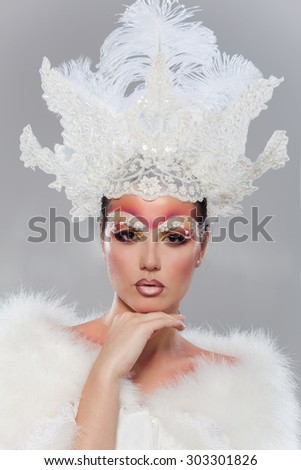 Close-up studio portrait of a girl in a fur collar and crown of the Snow Queen. Bright make-up  with pearls.