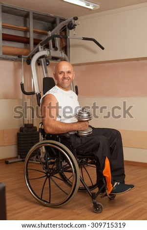 Happy disabled person in the gym doing exercises with dumbbells.