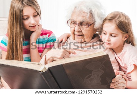 Grandmother with granddaughters looking old photos in brown family photo album together