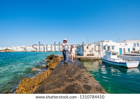 Woman together with child girl walking along the stone pier at sunny hot day, Naoussa, Paros island, Greece