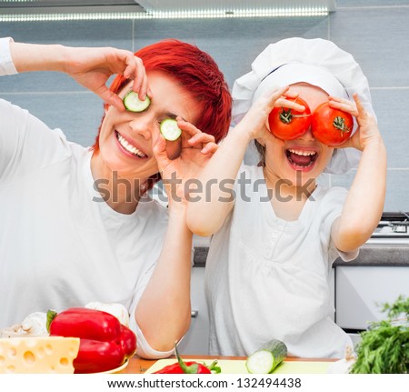 Mother And Funny Daughter Playing In The Kitchen With Vegetables