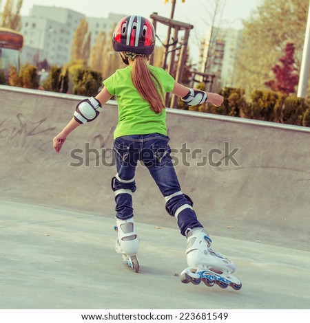 Back view of little girl in helmet on roller-skates in park
