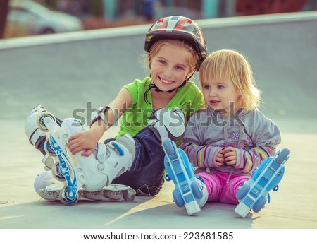 two beautiful little sisters in a roller skates sitting  on the street