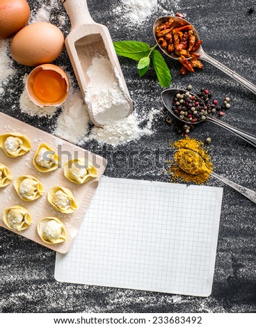 raw ravioli, different products and white sheet of paper for the recipe on the black kitchen table