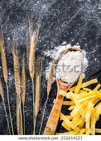 spikelets of wheat, pasta and spoon with flour  on a black  textured table