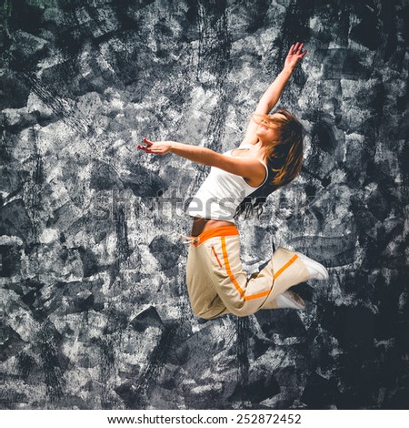 Young woman dancer jumping. On grunge wall background.