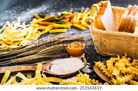 uncooked pasta, bread and other products on a black  textured table