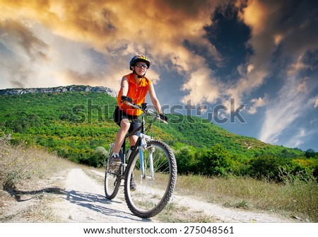 young athletic girl rides a bicycle on a mountain road at sunset