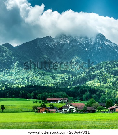 village near forest in mountains with peaks in clouds