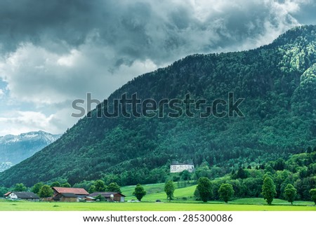 village near forest in mountains with peaks in clouds