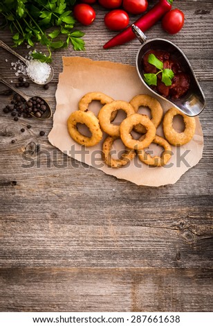 fried onion rings on parchment with sauce and vegetables on a wooden background