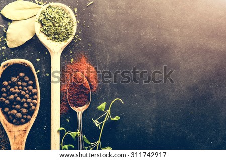 wooden spoons with spices and herbs on textured black background