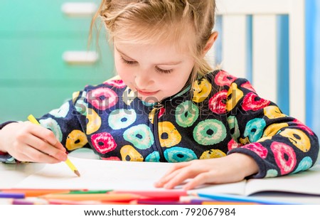 Cute little blonde girl draws a picture with colorful pencils