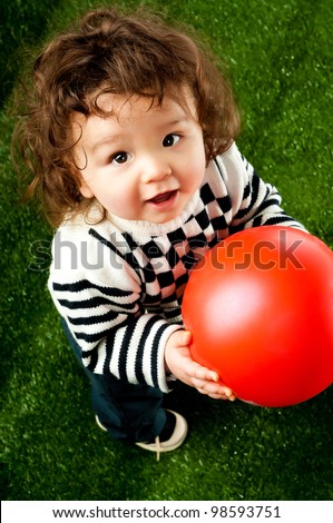 little kid with a red ball on the green grass
