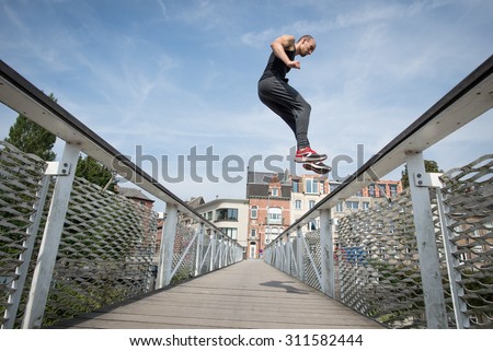 Man practices parkour and free running outdoor by doing a precision jump on a bridge