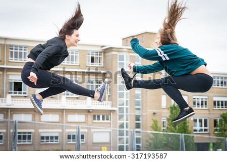 2 girls dancing and jumping up in the air in a city at school