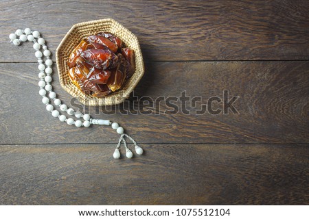 Table top view aerial image of decoration Ramadan Kareem holiday background.Flat lay date in wood basket with white rosary on modern rustic brown wood at office desk.Free space creative design text.